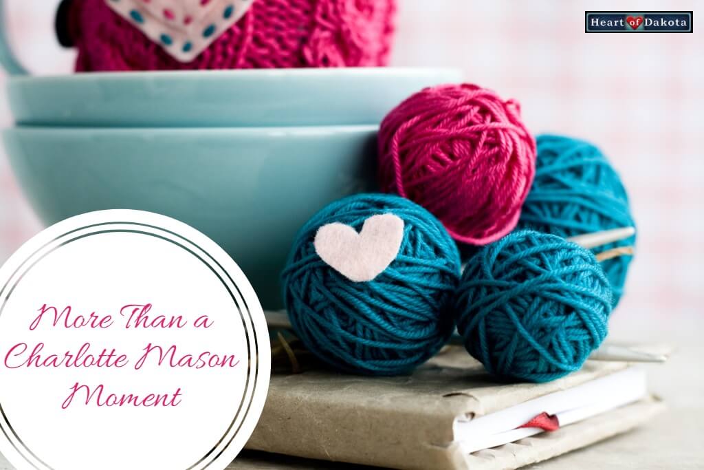 Red and blue balls of yarn sitting atop a book on a tabletop. A white paper heart is pinned to one of the balls. To the left, inside a white circle, text reads: "More Than a Charlotte Mason Moment."